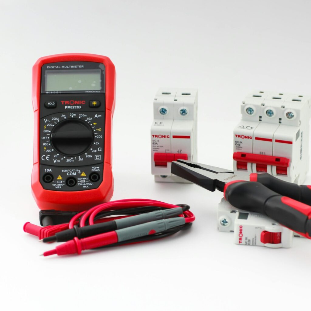 Close-up of a digital multimeter with electrical tools and circuit breakers on a white background.