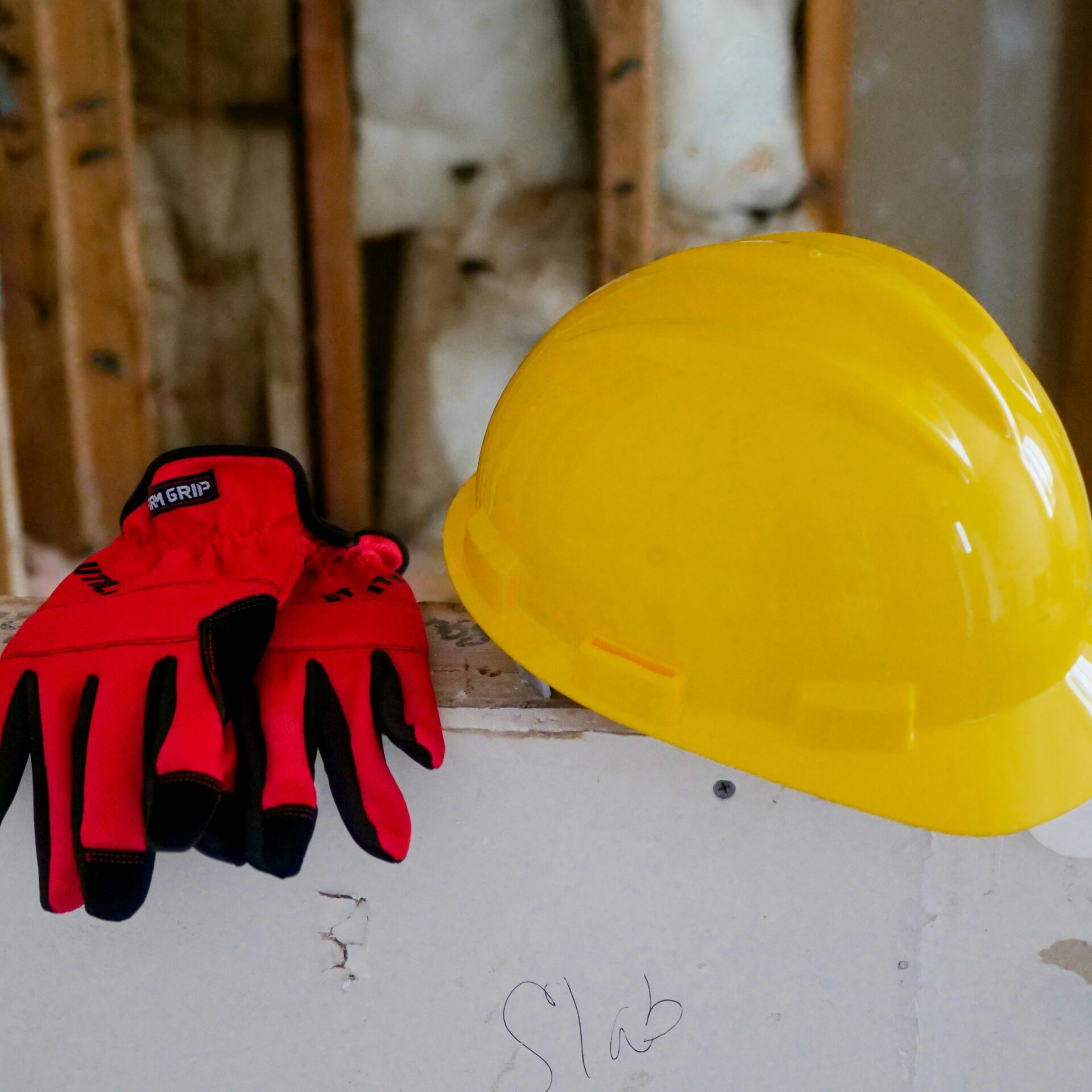 Close-up of a yellow hard hat and red gloves on a construction site, symbolizing safety and work.